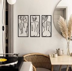 three paintings hang on the wall next to a table with chairs and a vase in front of it