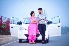 a man and woman standing next to a white car