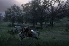 a man riding on the back of a white horse through a lush green forest filled with trees