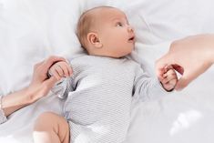 a baby laying on top of a bed next to an adult's arm and foot