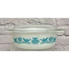 a glass casserole with blue birds and flowers on the bottom is sitting in front of a brick wall