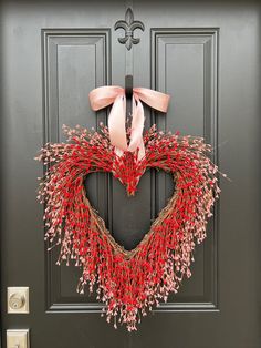 a heart shaped wreath with pink ribbon hanging on the front door to a black door