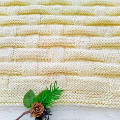 a knitted blanket is shown with a flower on the edge and green leaves in front