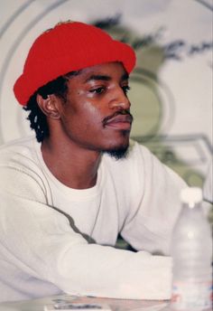 a man wearing a red hat sitting at a table with a bottle of water in front of him