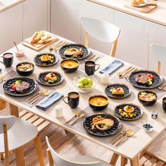 a dining table set with black plates and bowls filled with different types of food on it