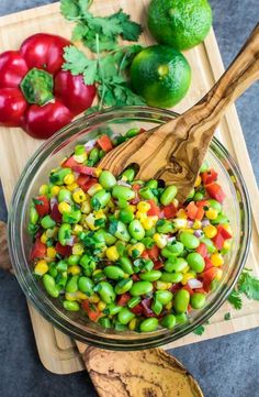 a wooden spoon in a glass bowl filled with green beans and tomatoes next to limes