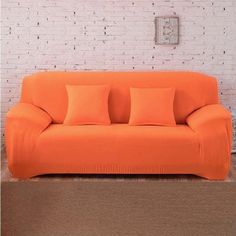 an orange couch sitting in front of a white brick wall with four pillows on it