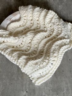 a white knitted blanket laying on top of a cement floor next to a blow dryer