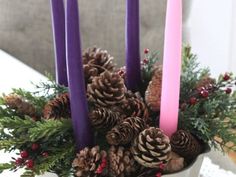 a white bowl filled with pine cones and purple candles