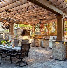 an outdoor kitchen and dining area with lights strung from the ceiling over the grills