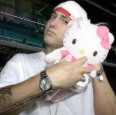 a man holding a hello kitty stuffed animal in his right hand and looking at the camera