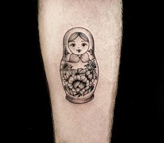 a black and white photo of a russian doll with grapes in a vase tattoo on the leg