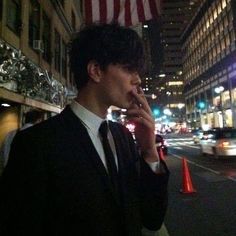 a man standing on the side of a street talking on a cell phone with an american flag in the background