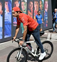 a man riding a bike in front of a wall with pictures on it and people walking around