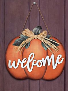 a wooden sign that says welcome with two pumpkins hanging from it's side