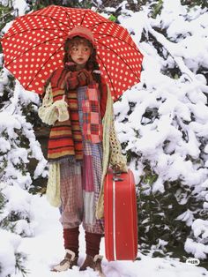 a woman with an umbrella and suitcase standing in the snow holding a red polka dot umbrella