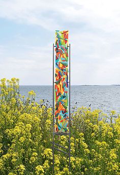 a tall metal sculpture sitting on top of a lush green field next to the ocean