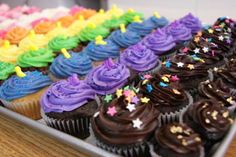 cupcakes with rainbow frosting and sprinkles in a tray on a table