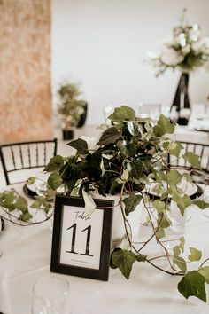 the table is set for an event with greenery and place cards on it, along with wine glasses