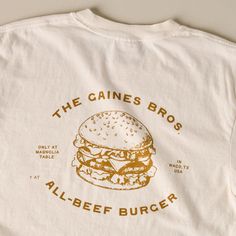 Show off your support for one of the best burgers in town with this classic ivory tee! Inspired by the fan-favorite Gaines Brothers Burger at Magnolia Table, this white tee features a playful, contrasting burger graphic that reads THE GAINES BROS ALL-BEEF BURGER. Retro Tee Design, Restaurant Tshirt Designs, Graphic Tee Inspo Design, Coffee Shop Tshirt, Burger Graphic, Lemon Shirt, The Best Burgers, Best Burgers, Magnolia Table