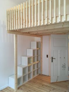 a room with wooden floors and white shelves under a lofted bed above the stairs