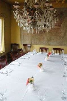 a dining room table with white linens and chandelier hanging from the ceiling