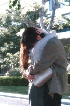 a man and woman embracing each other on the sidewalk in front of trees with buildings behind them