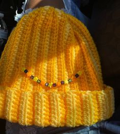 a yellow knitted beanie with small beads on the front and side, sitting in someone's lap