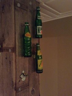 two green beer bottles hanging from the ceiling next to a wooden door with holes in it