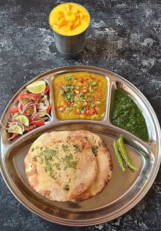 a metal plate topped with food next to a bowl filled with vegetables and sauces