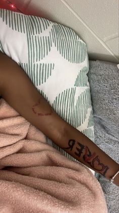 a woman with a tattoo on her arm laying in bed next to a pink blanket