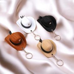 three hats with chains attached to them laying on a white satin surface, one is wearing a hat and the other has a keychain