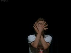 a man covering his face with both hands while standing in front of a black background