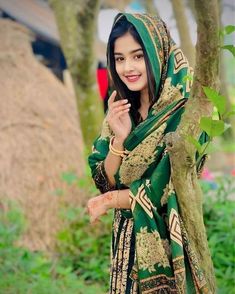 a woman standing next to a tree wearing a green and gold sari