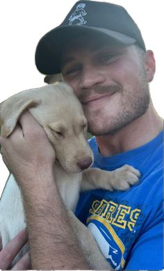 a man holding a puppy in his arms and smiling at the camera while wearing a hat