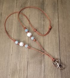 a brown cord with white and blue beads is on a wooden floor next to a pair of scissors