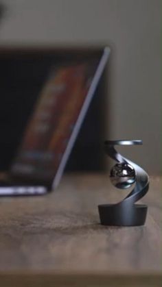 a laptop computer sitting on top of a wooden table next to a metal object with a spiral design