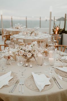 the table is set with white flowers and candles for an elegant wedding reception at the beach