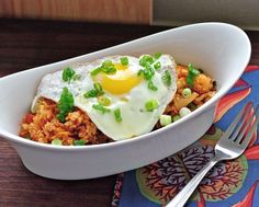 an egg on top of rice in a white bowl next to a fork and napkin