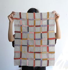 a woman holding up a piece of cloth with squares on it and the fabric is multicolored