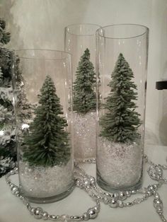 three glass vases filled with snow and trees on top of a table next to a christmas tree