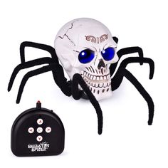 a skull with blue eyes sitting next to a remote control and a toy spider on it's back