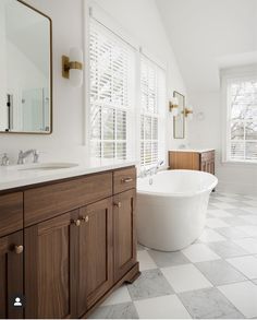 a large white bath tub sitting next to a bathroom sink under a mirror on top of a wooden cabinet