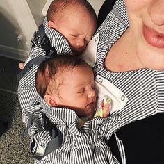 a woman holding two babys in her arms while they are wearing black and white stripped shirts