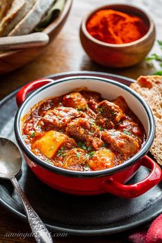 a red pot filled with stew next to bread