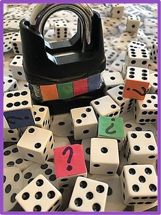 a pile of dice with numbers on them sitting next to a black container filled with question marks