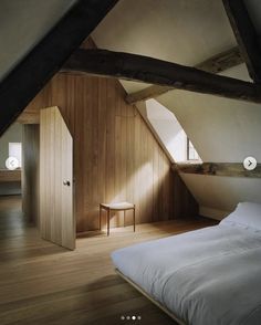 an attic bedroom with wood paneling and white bedding, along with a chair