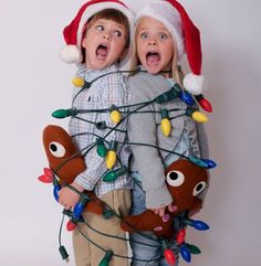 two children wearing christmas lights and santa hats, standing next to each other with their mouths open