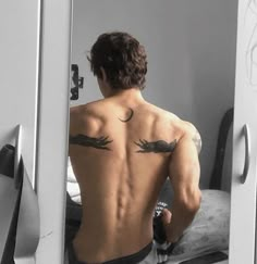 a man with tattoos on his back looking at himself in the mirror