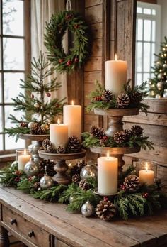 christmas candles are arranged on a table with pine cones and evergreen branches in the center